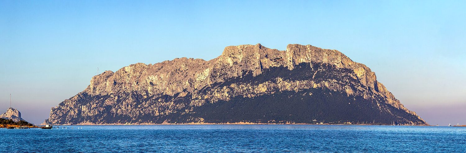 L'isola di Tavolara vista da Porto Istana con la luce bassa del tramonto che accende di rosa la parete rocciosa, sopra un mare calmo